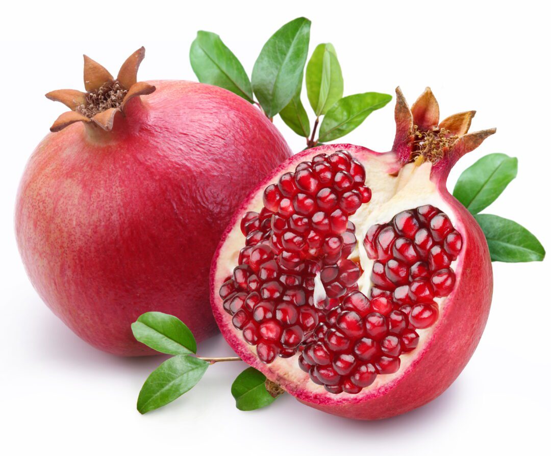 Whole and cut pomegranates with red seeds and green leaves