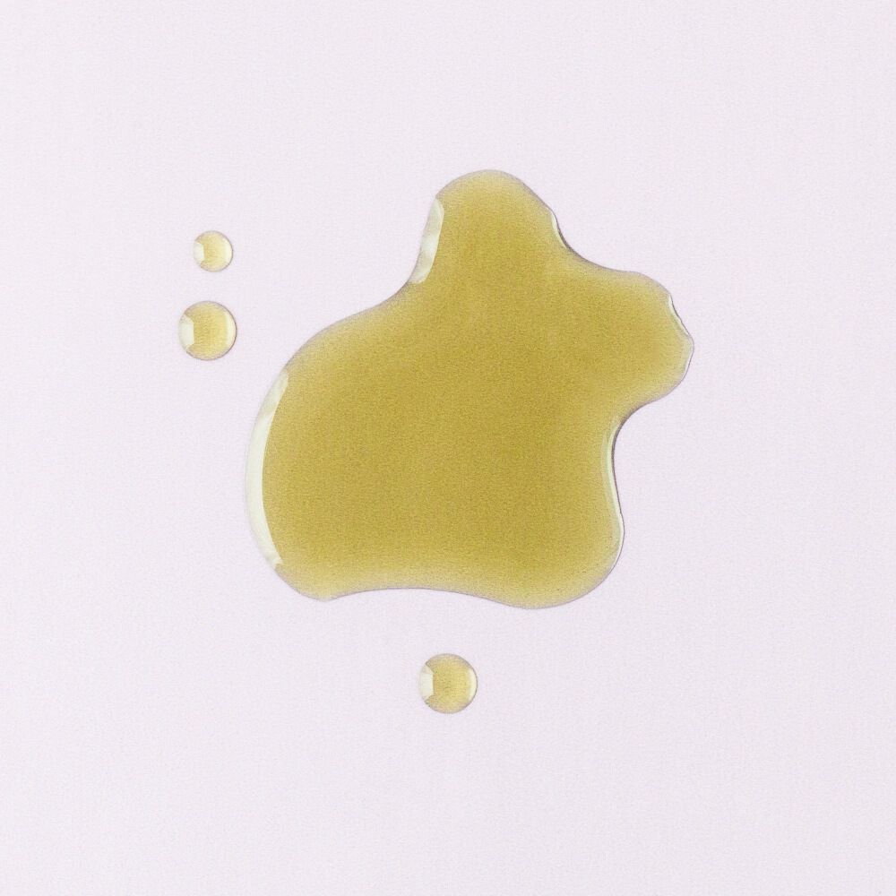 Golden-green tamanu oil droplets on a pale background