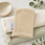 Pearls of Nature natural sisal soap saver sack resting on folded cream and sage towels with a ceramic dish and eucalyptus nearby.