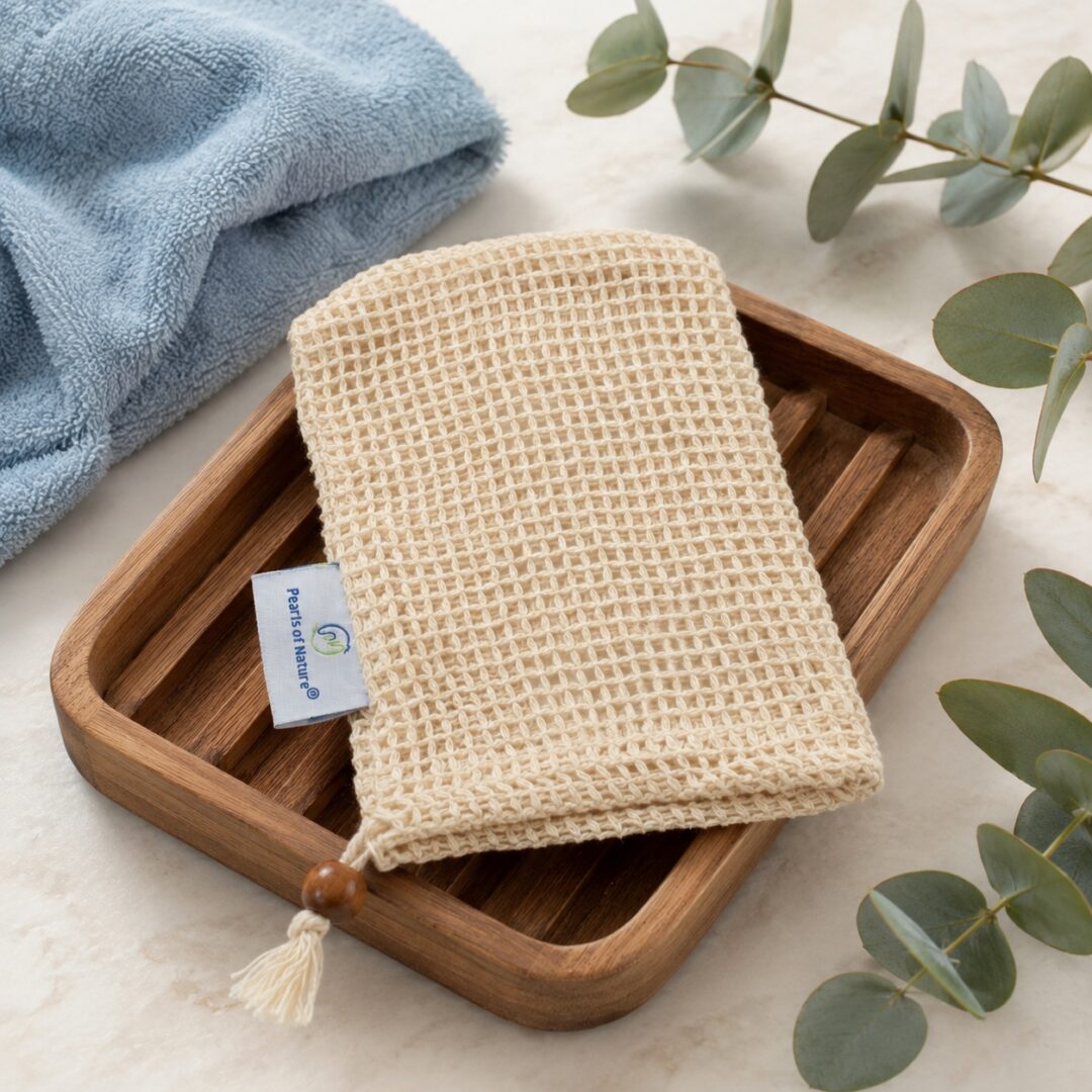Pearls of Nature natural sisal soap saver sack on a wooden soap dish with a blue towel and eucalyptus accents.