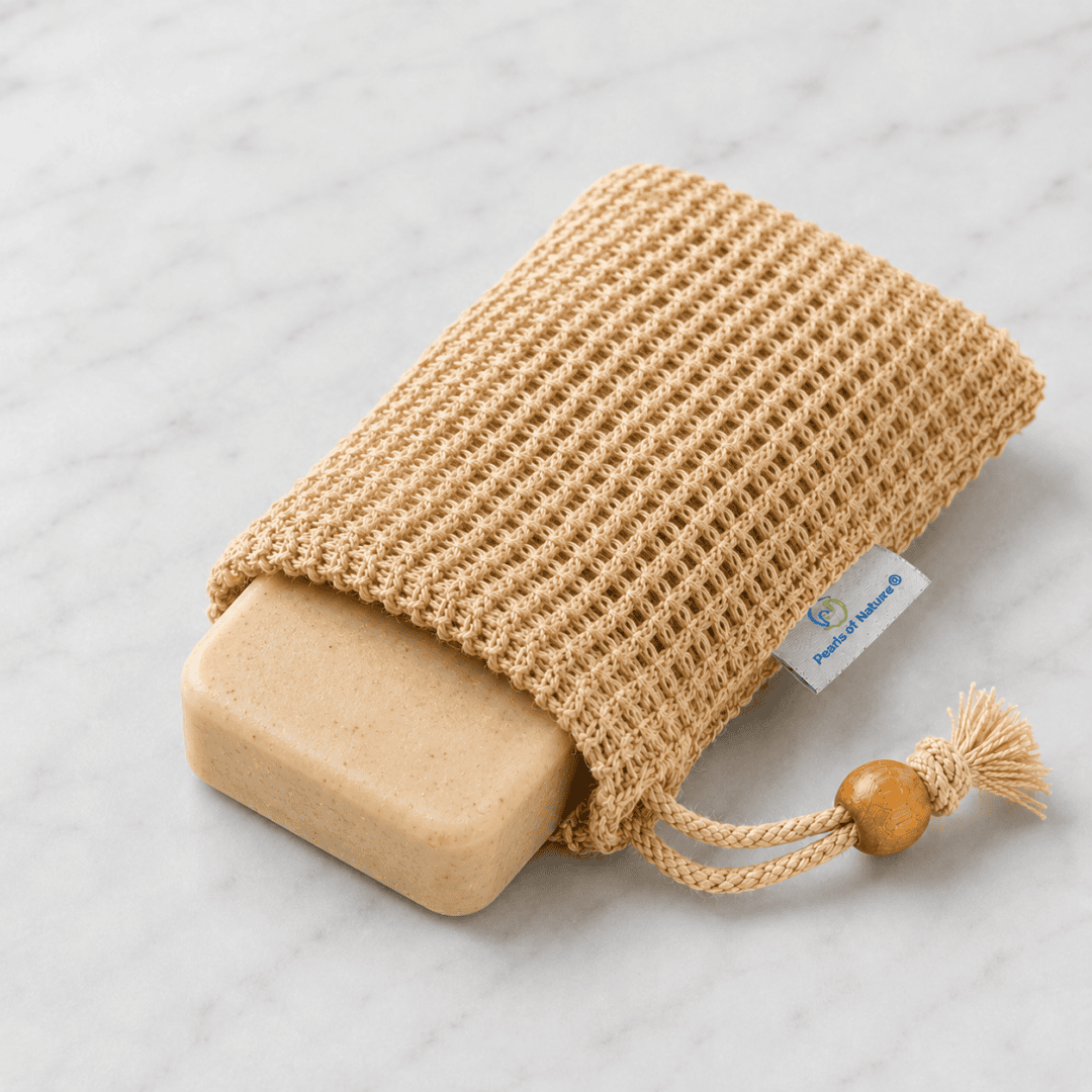 Pearls of Nature sisal soap saver sack holding a rounded oatmeal-colored soap bar on a clean white marble surface.